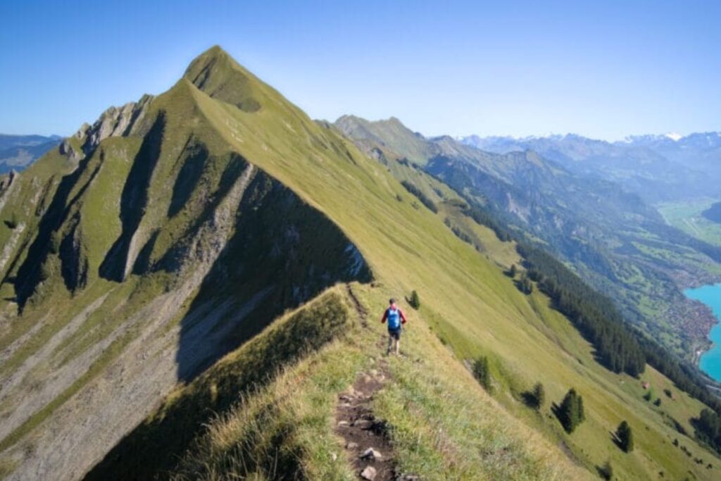Randonneur progressant sur une portion de crête exposée du Hardergrat, pentes herbeuses de part et d’autre