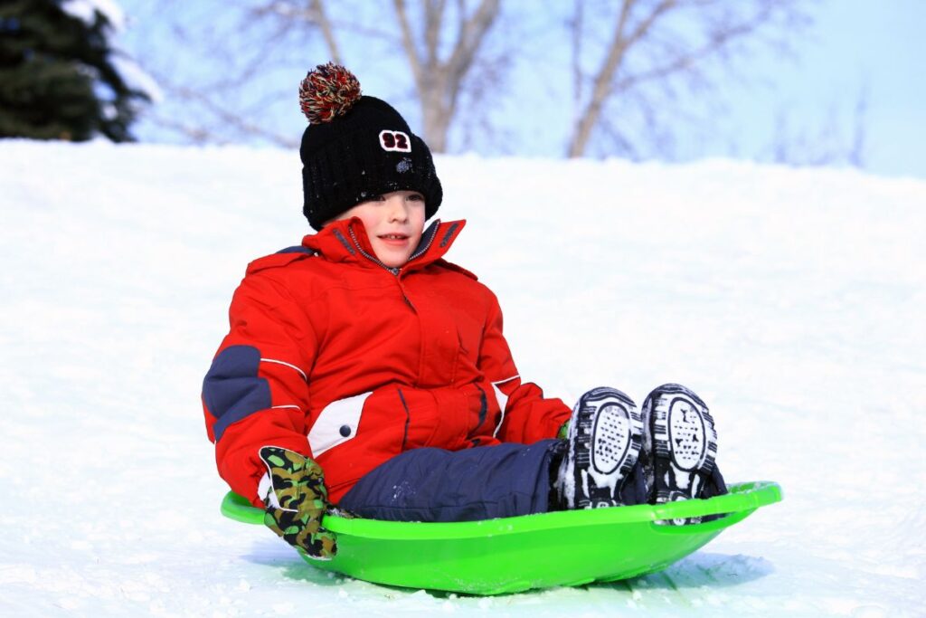 Enfant en combinaison de ski assis sur une luge au sommet d’une pente enneigée ensoleillée