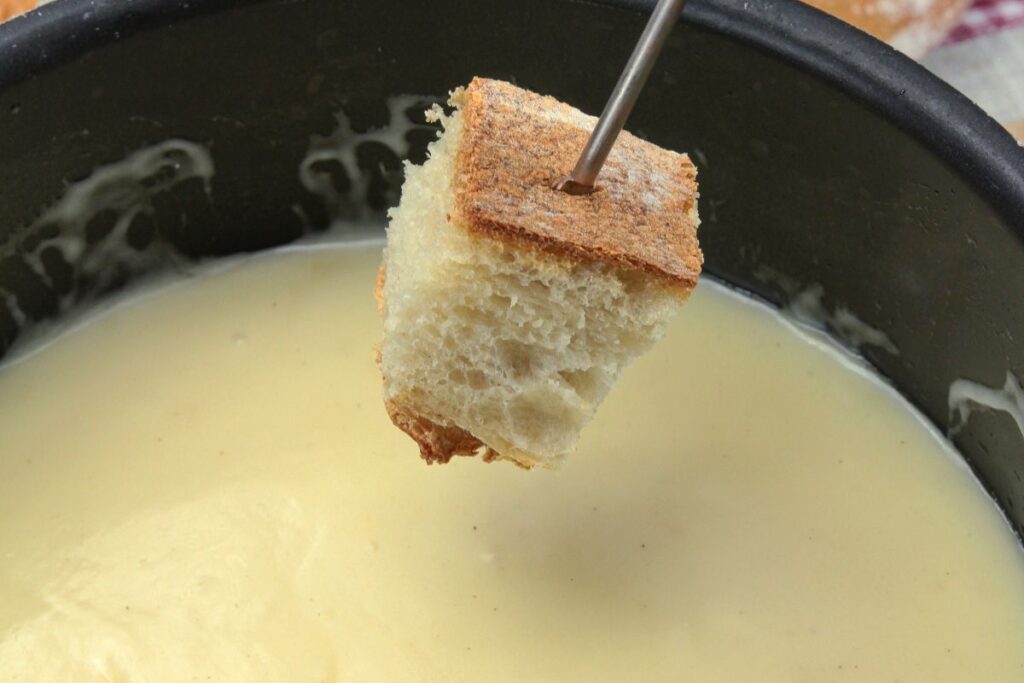 Fondue savoyarde dans un caquelon avec morceaux de pain piqués sur des fourchettes