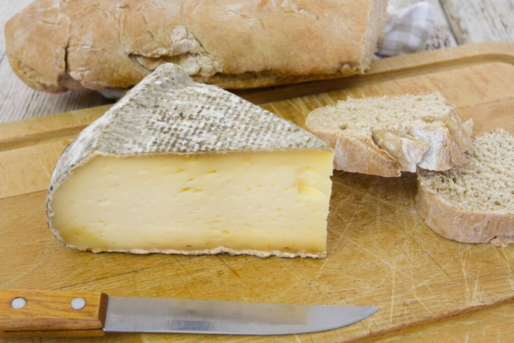 Tomme de Savoie à la croûte grise et à la pâte crème, coupée sur une planche