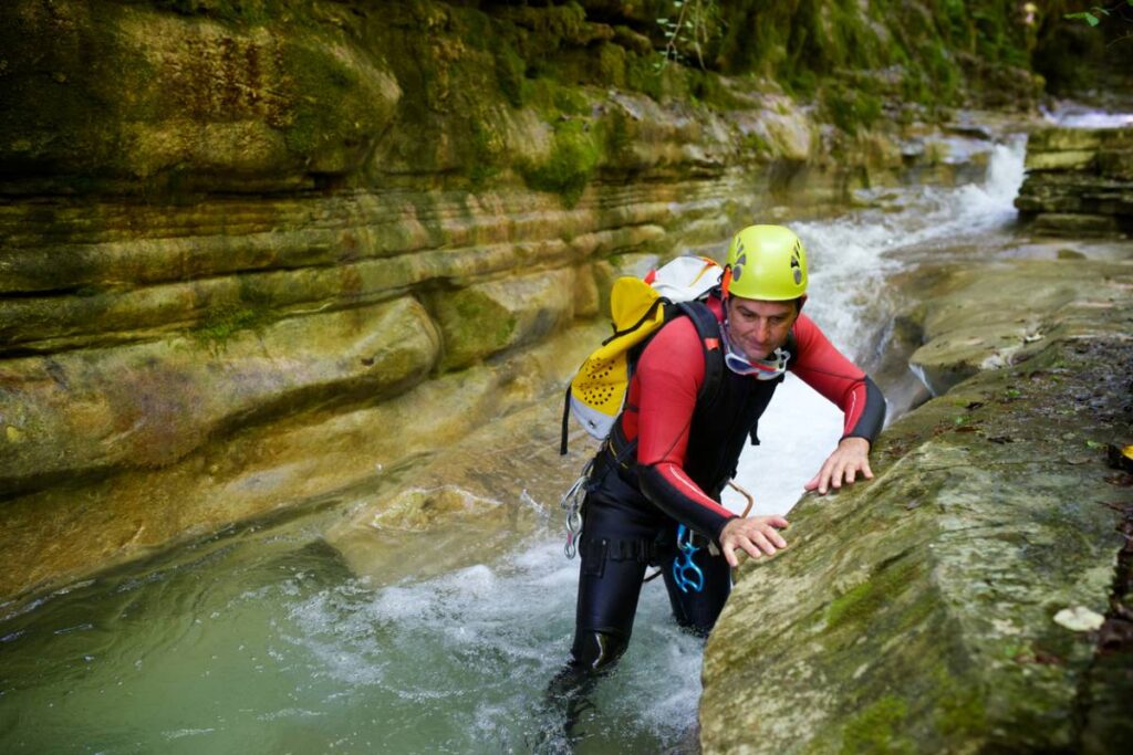 Débutants en combinaison néoprène et casque descendant une cascade en rappel lors d’une sortie canyoning