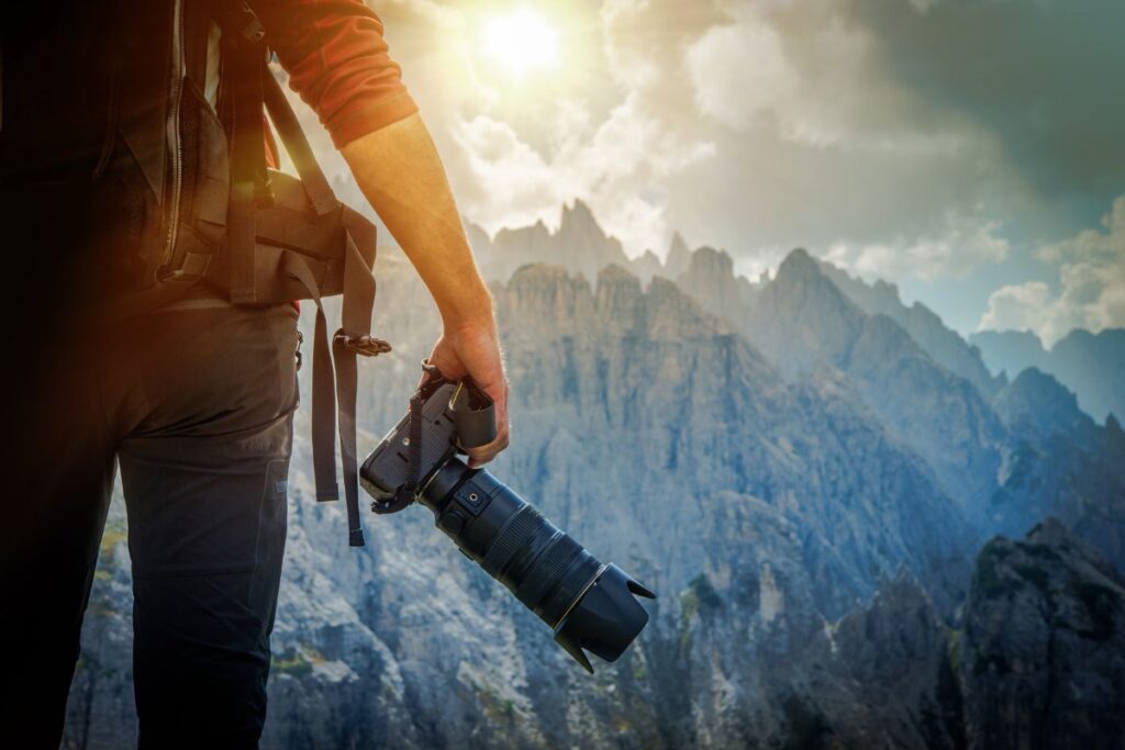 Appareil photo reflex tenu par un randonneur face à un paysage de montagne