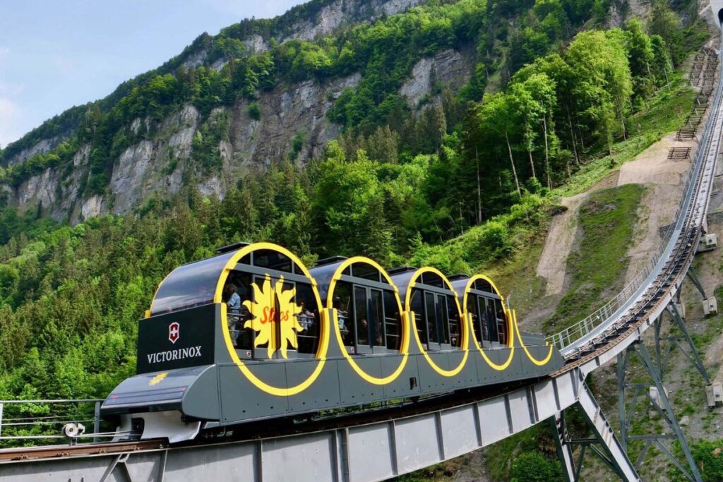Cabines cylindriques rouges du funiculaire de Stoos gravissant la pente boisée au-dessus de Schwyz