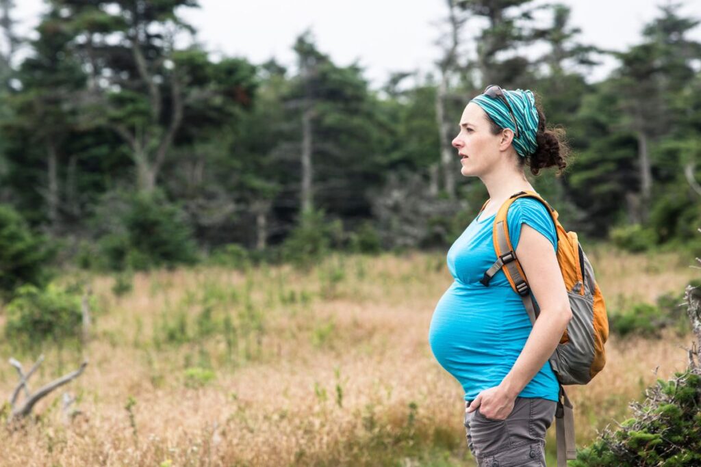 Future maman faisant une pause assise au bord d’un sentier de randonnée de moyenne montagne