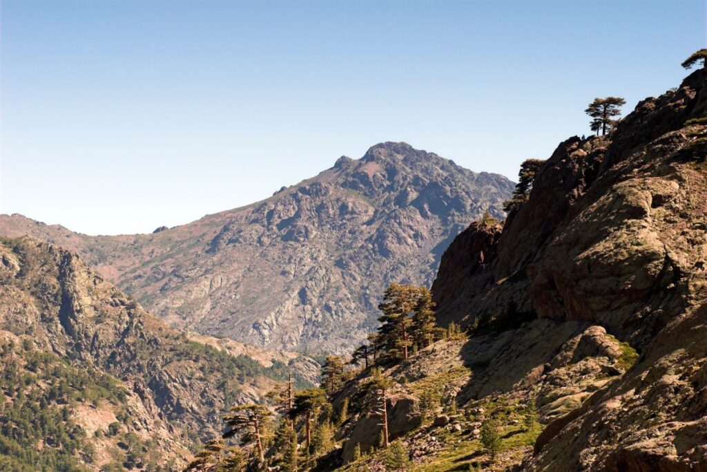 Randonneur fatigué assis sur un rocher face aux montagnes du GR20