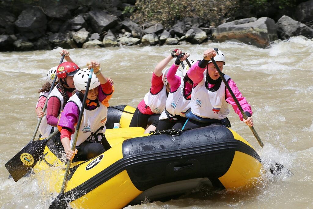 Équipage de rafting en combinaisons néoprène, casques et gilets, pagayant ensemble sur une rivière