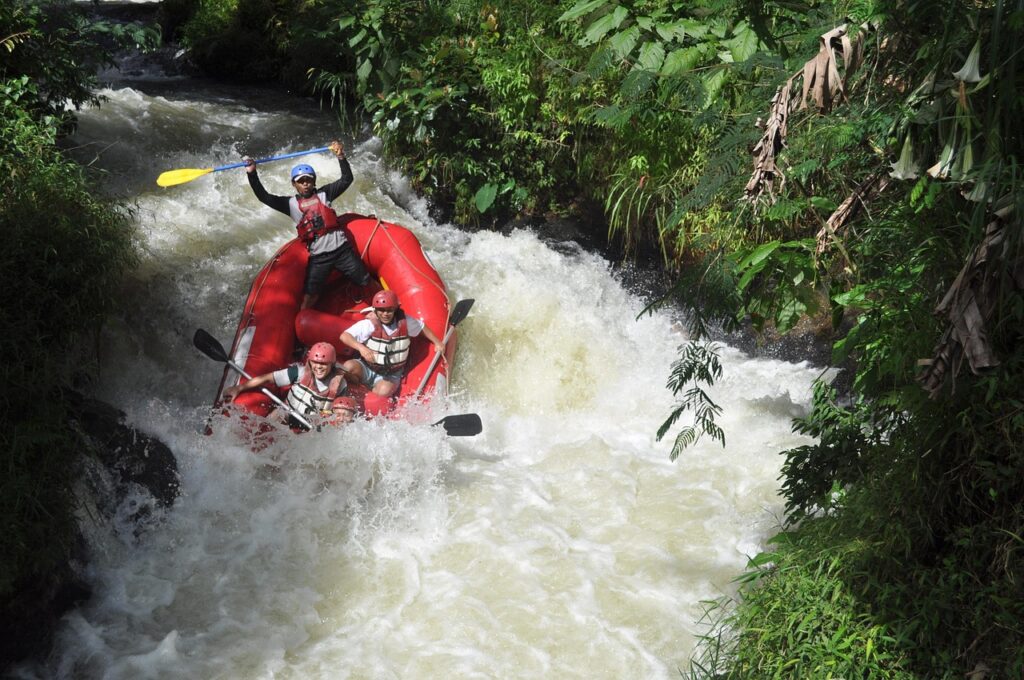 Raft pneumatique franchissant un rapide sur une rivière de montagne, entouré de forêts et de reliefs alpins